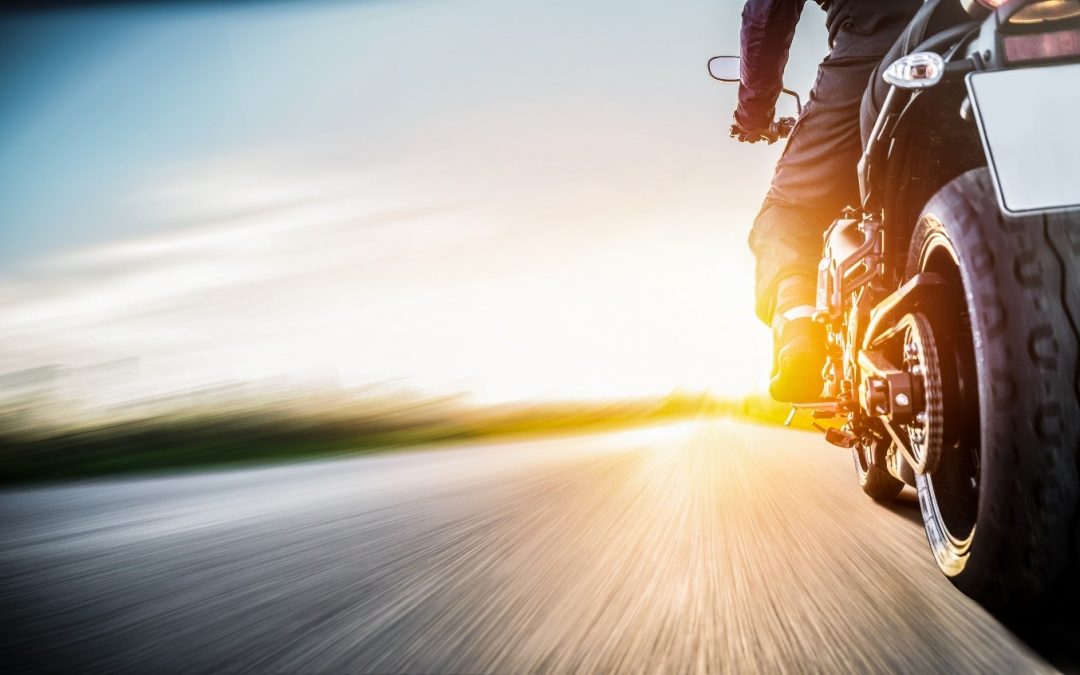 bottom half of motorcycle speeding down the road toward the sunrise, the driver is going fast enough to make the road blurry